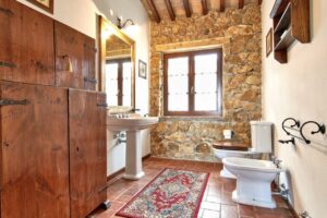 Bagno rustico in pietra con lavabo bianco e mobile in legno, prestigioso casale.