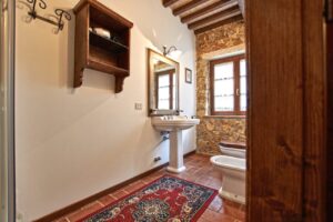 Vista di bagno rustico in prestigioso casale con legno, pavimento rosso e travi a vista.