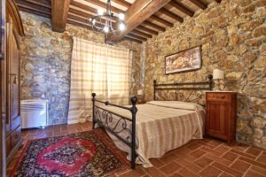 Accogliente camera rustica elegante in prestigioso casale con pietra, letto nero e travi a vista.