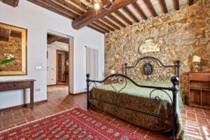 Camera da letto rustica ed elegante in prestigioso casale con pietra, travi e letto in ferro.