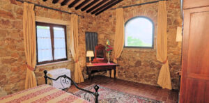 Accogliente camera rustica in pietra con tende gialle e letto rosso, prestigioso casale.