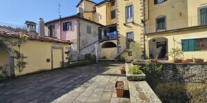 Cortile rustico con giardino pensile sulle mura a Castelnuovo di Garfagnana, edifici dai toni caldi.