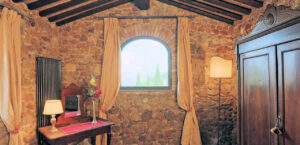 Prestigioso casale in pietra e legno con finestra ad arco e travi a vista.
