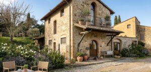 Casa di campagna in pietra con balcone fiorito, giardino curato e sedie nel vialetto