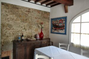 Sala da pranzo rustica con parete in pietra, travi a vista e finestra ad arco