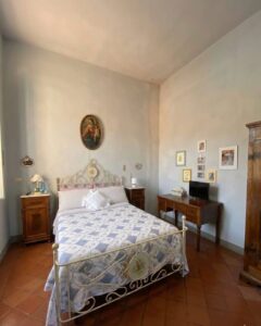 Camera da letto blu grigio con letto bianco, comodini, scrivania e armadio in legno.