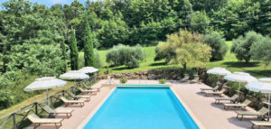 Prestigioso casale: piscina blu, lettini e ombrelloni bianchi per un relax esclusivo tra il verde.