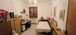 Cameretta piccola con letto singolo, scrivania, armadi e mensole giochi.