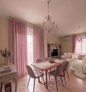 Tavolo da pranzo moderno, sofà rosa e crema, luce soffusa nel living.