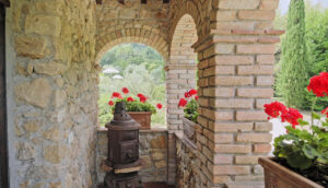 Arco in pietra con fiori rossi al Prestigioso Casale e vasi su lati.