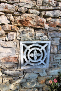 Muro in pietra con grata decorativa, villa storica dominante con parco e piscina panoramica.