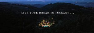 Vista notturna di un borgo toscano con prestigioso casale tra colline e calde luci sotto le stelle.