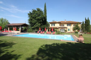 Villa toscana con piscina, giardino mediterraneo, lettini rossi e cipressi