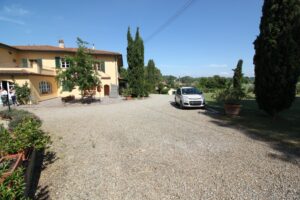 Villa di campagna toscana con cortile in ghiaia, cipressi e auto parcheggiata