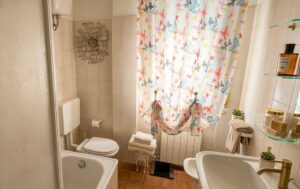 Bagno vintage con tubo bianco e mobiletto in pedaliera, luci naturali e florale.