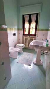 Bagno vintage con bidet, vasca pedestal e finestra classica in verde pastello.