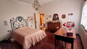 Una camera vintage 1920 con letto ornato, mobili in noce e riflessi sul parquet scuro.