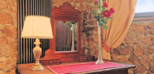 Elegante cassettone in legno scuro con specchio, lampada e rose rosse in prestigioso casale.