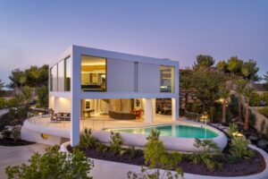 Villa moderna su due livelli con piscina e terrazza immersa in una collina verdeggiante al crepuscolo.