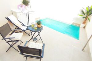 Zona relax moderna con piscina, sedie di design e piante su patio in cemento.