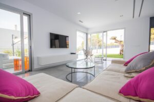 Salotto moderno minimalista con divano bianco, cuscini fucsia e ampie vetrate sulla piscina.