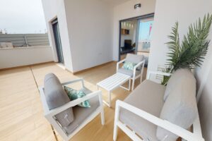Terrazzo moderno arredato con divano bianco, poltrone grigie, tavolino e piante artificiali.