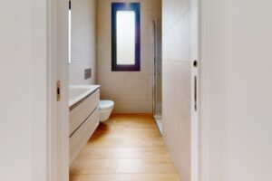 Bagno moderno con lavabo in legno, doccia in vetro e finestra tonda.