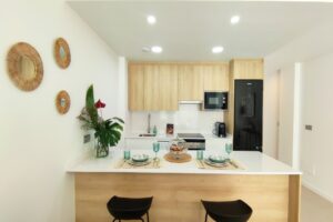 Cucina moderna e luminosa in open space con isola, tavolo apparecchiato e frigorifero nero.