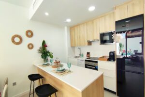 Moderna cucina luminosa con isola in legno chiaro, elettrodomestici a incasso e zona pranzo.