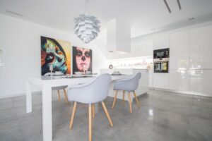 Sala da pranzo moderna e cucina minimalista bianca con tavolo di design e quadri colorati.