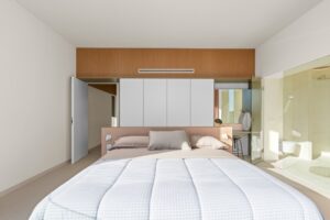 Camera da letto moderna con letto matrimoniale, armadi a muro e bagno in vetro a vista.