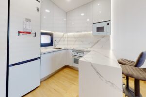 Cucina moderna minimalista con mobili bianchi, ripiani in marmo e bancone colazione in legno.