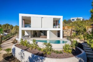 Casa moderna bianca a due piani con piscina e grandi vetrate in mezzo al bosco.